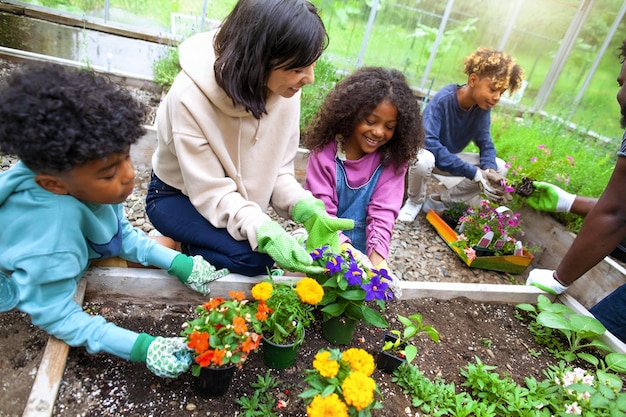 A teacher facilitates a group of elementary school students working on a community garden project. They are planting flowers and vegetables, with gardening tools visible.