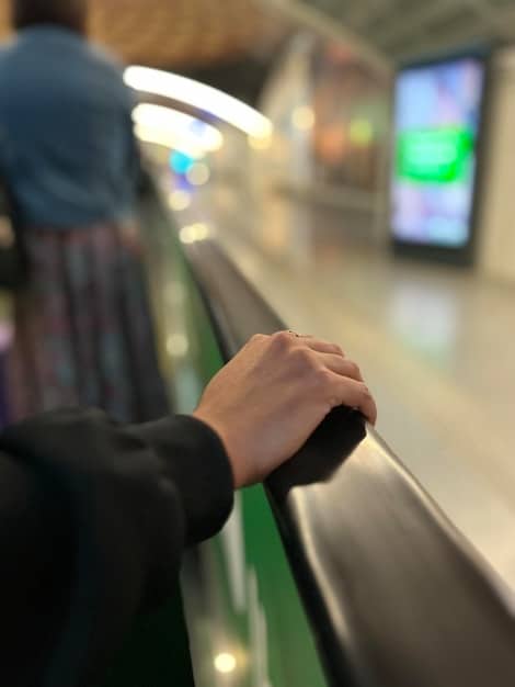 An employee swiping a transit card at a subway station turnstile, highlighting the pre-tax payment method. A blurred background shows other commuters and station signs to give context.